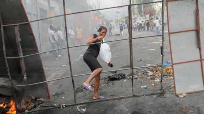 Wanita melintas brigade saat protes di Haiti.